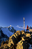 Hiker at cross on summit of Großer Troegler with view to Wilder Pfaff and Zuckerhuetl Mountains, Stubai Mountain Range, Tyrol, Austria