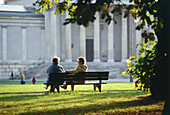 Älteres Paar sitzt auf einer Parkbank am Königsplatz, München, Bayern, Deutschland