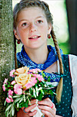 Teenage girl in traditonal dress holding a bunch of flowers, Irsee, Bavaria, Germany