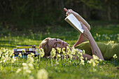 Young woman lying on meadow while reading a book, Icking, Bavaria, Germany