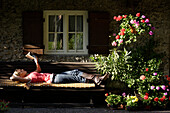 Junge Frau liegt auf einer Band und liest ein Buch, Branennburg, Oberbayern, Bayern, Deutschland