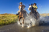 Cowboy and cowgirl riding through creek, wild west, Oregon, USA