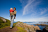 Mutter trägt Kleinkind auf Wanderung, Bei Kalle, Schärenlandschaft, Insel Austvagoya, Lofoten, Norwegen