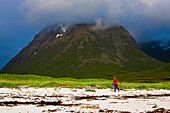 A woman walking along the beach in rainclothes, Hadselsand, Lofoten, Norway