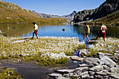 A young woman and two young men about to bath, swim in a mountain lake, cotton gras in the foreground, Laghi della Valletta, Gotthard Region, canton of Tessin, Ticino, Switzerland