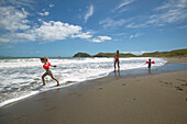 Kinder spielen mit ihrer Mutter am Strand von Port Jackson, an Nordspitze der Coromandel Peninsula, Nordinsel, Neuseeland