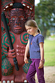 Girl leaning on wooden Maori sculpture, Waitangi Maori Museum, Waitangi, Bay of Islands, Northland, North Island, New Zealand