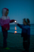 Two girls (2-5 years) standing at beach Kniepsand, moon between them, Wittduen, Amrum island, North Frisian Islands, Schleswig-Holstein, Germany