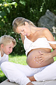 Junge (4-5 Jahre) betrachtet Schwangerschaftsbauch seiner Mutter, Steiermark, Österreich