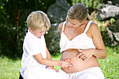 Junge (4-5 Jahre) malt Sonne auf Bauch einer schwangeren Frau, Steiermark, Österreich