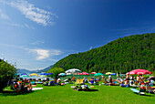 sunbathing area with sunshades and bathers at beach of lake Abersee, lake Wolfgangsee, Salzkammergut, Salzburg, Austria