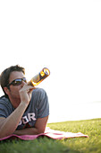 Mann liegt auf dem Bauch und trinkt Bier, Erholungsgelände Ambach, Starnberger See, Bayern, Deutschland