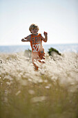 Boy running through meadow of shore grass, Sysne, Gotland, Sweden