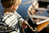 Junge (3-4 Jahre) hält Seil von einem Ruderboot, Staffelsee, Oberbayern, Bayern, Deutschland, MR
