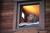 Young woman looking out of window of a alpine lodge, Heiligenblut, Hohe Tauern National Park, Carinthia, Austria
