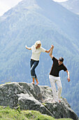 Junges Paar balanciert über einen Felsen, Heiligenblut, Nationalpark Hohe Tauern, Kärnten, Österreich