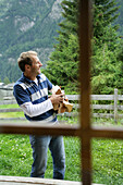 View through a window of a alp lodge to a man carrying logs, Heiligenblut, Hohe Tauern National Park, Carinthia, Austria