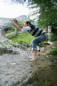 Mann spritzt mit Wasser an einem Gebirgsbach, Heiligenblut, Nationalpark Hohe Tauern, Kärnten, Österreich