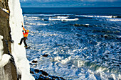 Ice climber in frozen waterfall above ocean, Kaldakinn, Iceland