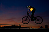 Trialbiker fährt auf einem Geländer bei Sonnenuntergang, Linz, Oberösterreich, Österreich