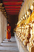 Young applicant monk in front of row of goldened Buddha statues at Wat Arun temple (Temple of the Dawn). Bangkok. Thailand