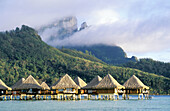Hotel bungalows on stilts over the lagoon, mountains in background. Bora Bora island, Leeward Islands. French Polynesia