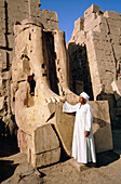 Warden by the remaining legs of a pharaon statue. Karnak temple. Luxor. Egypt