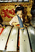 Child playing music at a gamelan (orchestra) Hinduist religious ceremony (odalan) in the Celuk Temple. Bali island. Indonesia