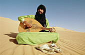 Baly, Tuareg singer and musician, sitting on an Erg Admer sand dune. Tassili n Ajjer desert. Sahara. South Algeria