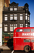 Red double-decker bus passing by Victorian house in black. London. England