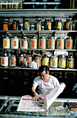 Herbalist reading newspaper in his shop. Macau. China