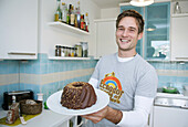 Lachender junger Mann hält einen Schokoladenkuchen, München, Deutschland