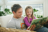 Father and daughter (3-4 years) reading a book, Munich, Germany
