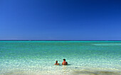 A couple sitting in shallow water on the beach of Heron Island, Great Barrier Reef, Australien