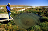 Tourist looking at The Bubbler, a mound spring in Wabma Kadarbu Mound Springs Conservation Park, Oodnadatta Track, South Australia, Australia