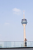 Rheinturm, Frau fotografiert im Vordergrund, Düsseldorf, Nordrhein-Westfalen, Deutschland