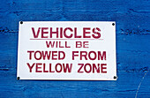 Sign on a blue wall. Vehicles will be towed from yellow zone . California
