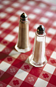 Vertical close up view of salt and pepper shakers on a red checkered table cloth