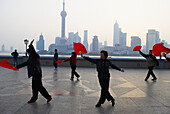 China. Shanghai. Chinese women dance with red fans on the bund in Shanghai for exercise every morning.
