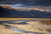 Storm clouds at sunset over Black Mountains and flooded salt pan, Devils Golf Course, Death Valley, California