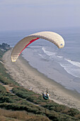 Paraglider over ocean beach and cliffs at Rincon Point, near Carpinteria, Santa Barbara County, California