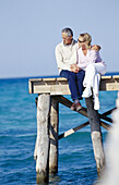 Couple sitting down in a wooden footbridge over the sea