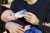  Adult, Adults, Affection, Aliment, Aliments, Babies, Baby, Caucasian, Caucasians, Child, Children, Color, Colour, Contemporary, Dad, Eat, Eating, Exterior, Families, Family, Father, Fathers, Feeding bottle, Feeding bottles, Fondness, Food, Growing, Growt