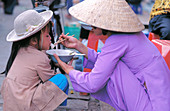 Woman feeding child noodles at market. Hanoi. Vietnam