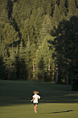 Girl, age 5, running grass area with forest in background. McCall, Idaho. USA