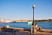 Eine Frau sitzt auf der Uferpromenade von Sliema mit Blick auf Valletta, Malta, Europa