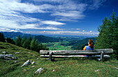 Frau sitzt auf Bank und blickt über Talkessel von Inzell, Kohleralm, Chiemgauer Alpen, Chiemgau, Bayern, Deutschland