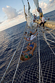 Passagiere entspannen sich im Bugspriet Netz vom Großsegler Star Flyer, Rangiroa, Tuamotu Inseln, Französisch Polynesien, Südsee