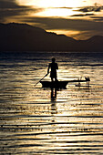 Man standing paddling in a canoo at sunset, New Britain, Papua New Guinea, Oceania