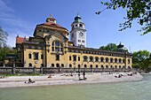People sunbathing at the shore of Isar river in front of Müllersches Volksbad, Munich, Bavaria, Germany